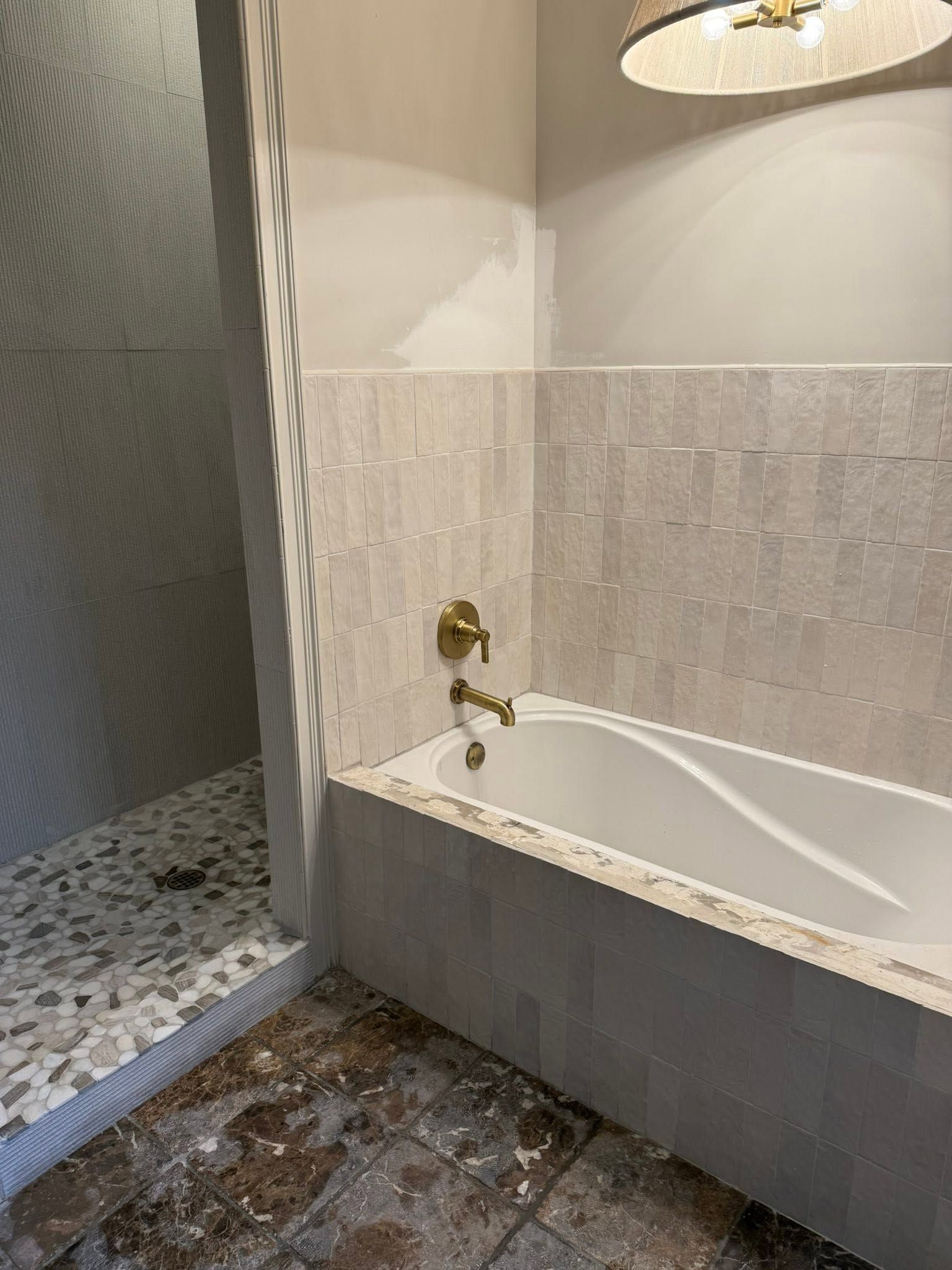 Bathroom with a white tub, brass faucet, tiled walls, and a pebble-floored shower area.
