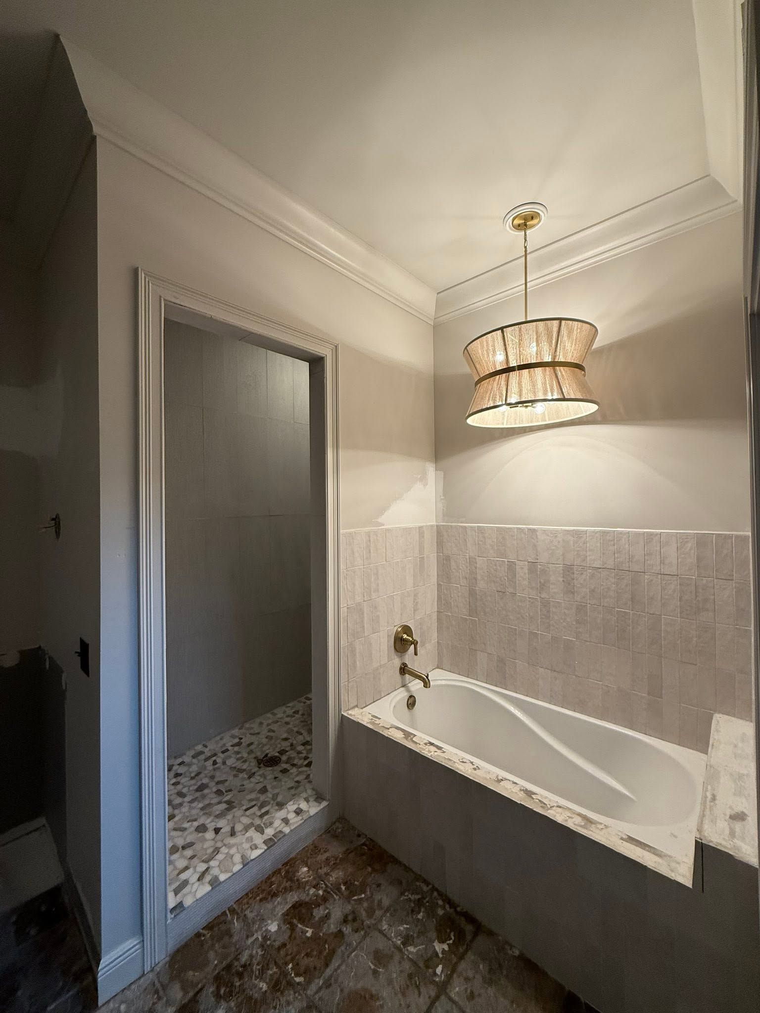 Bright bathroom with freestanding tub, tiled walls, and a hanging chandelier beside a glass shower door