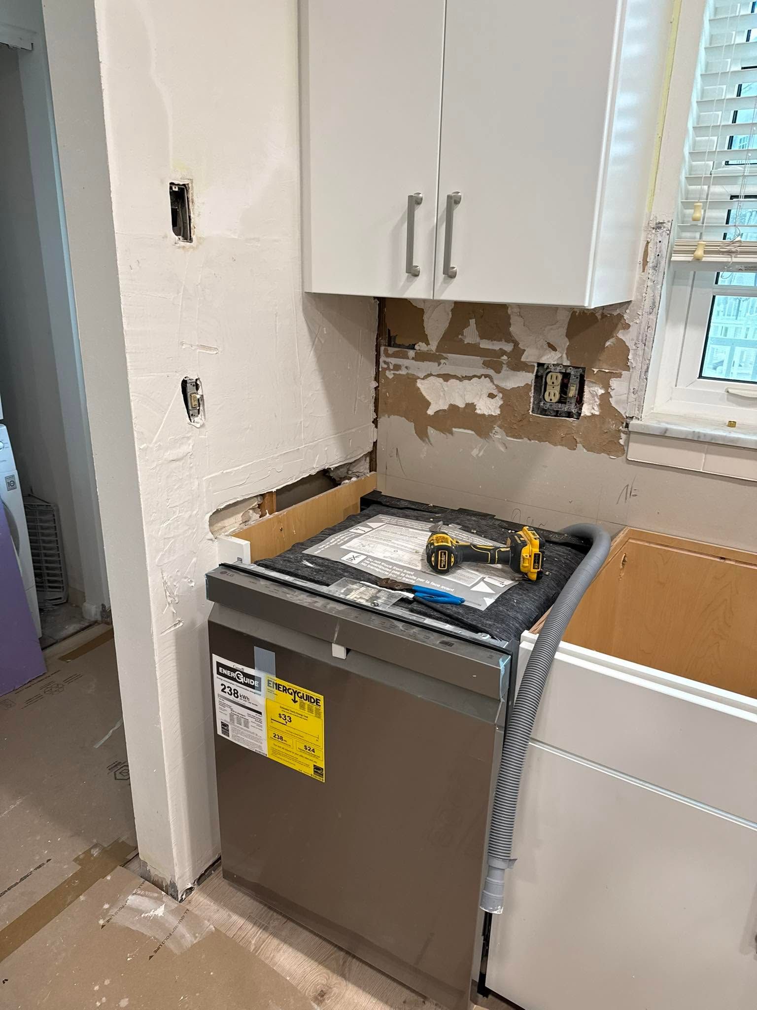 Kitchen under renovation with a dishwasher, open cabinet, exposed wall, and tools by the sink