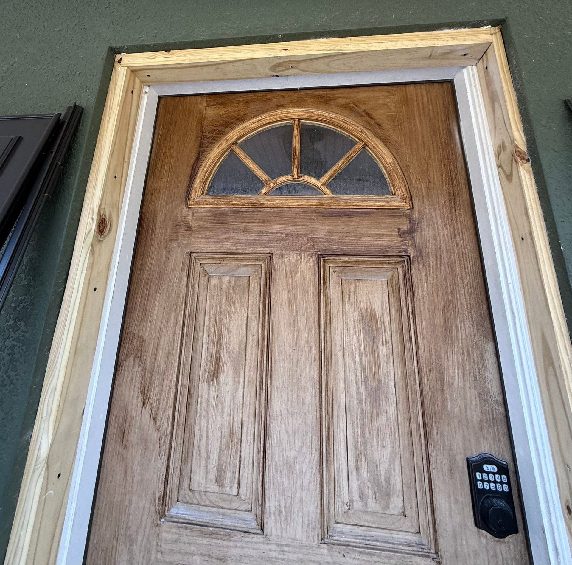 Wooden front door with an arched window and keypad lock on a light-colored house