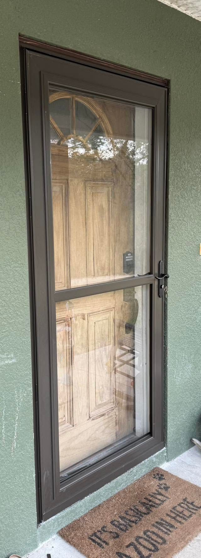 Brown front door with glass panels and a storm door on a green house exterior.