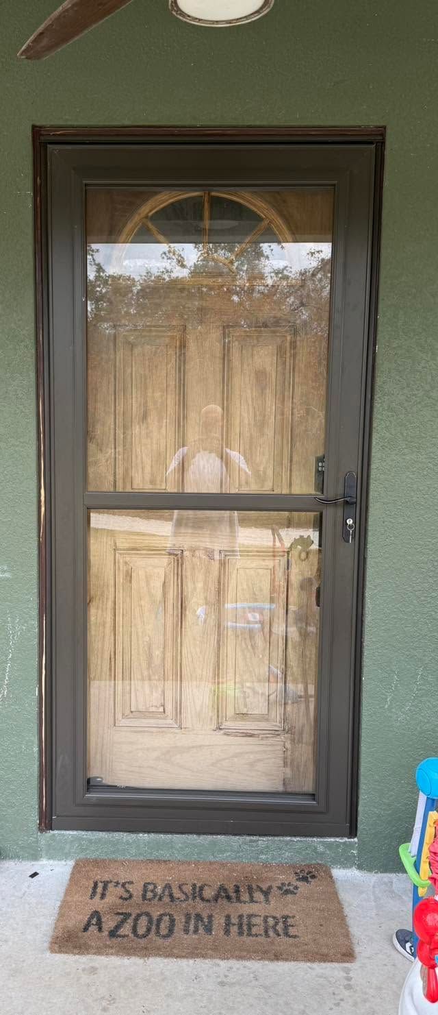 Front door with glass panel and a welcome mat on a green exterior wall.