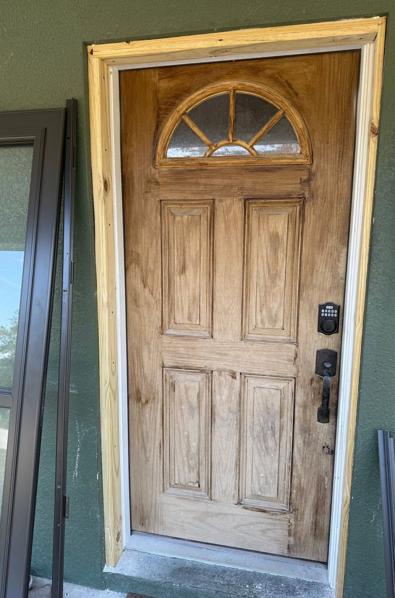 Weathered wooden front door with an arched window, set in a green exterior wall