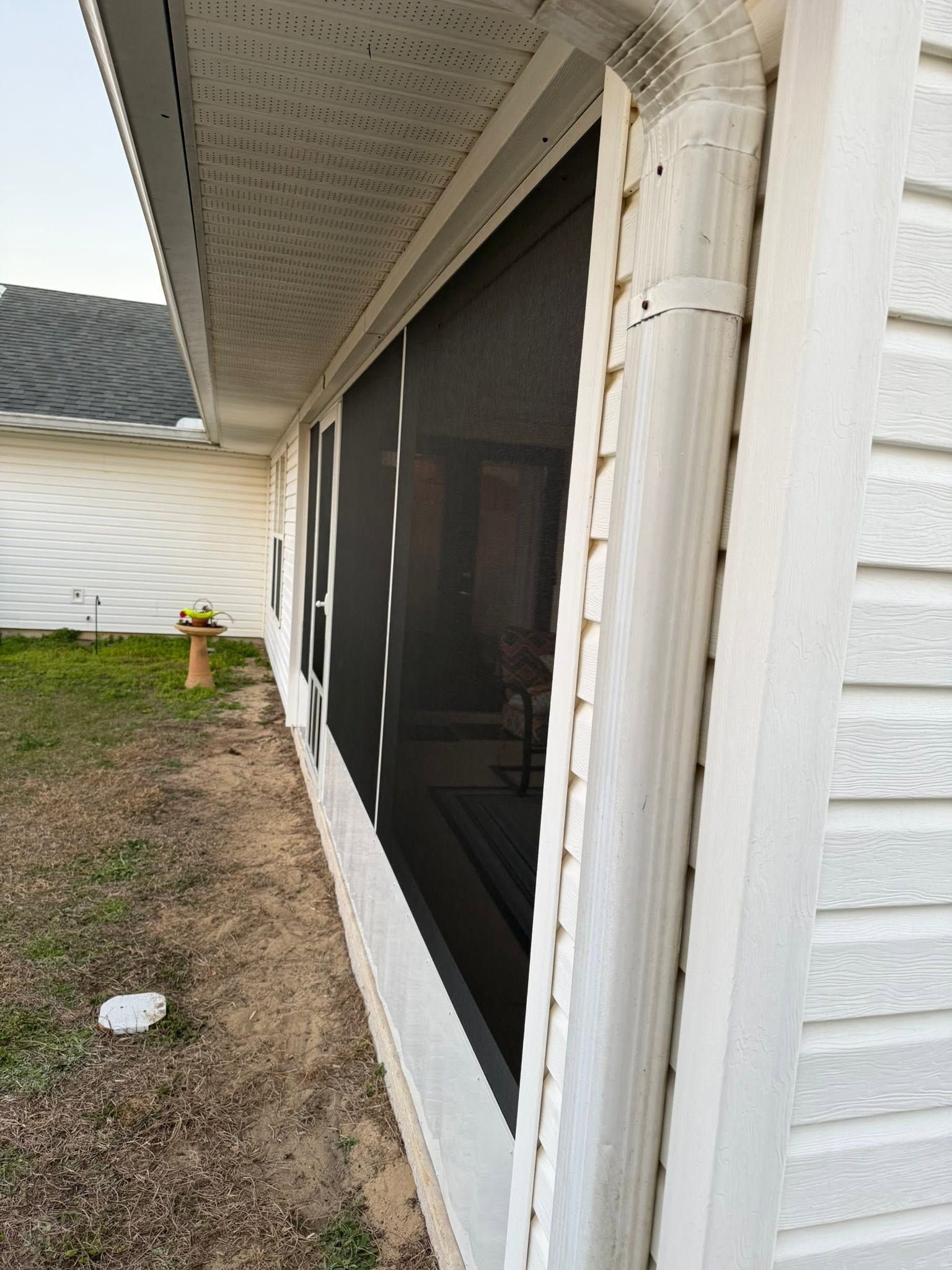 Screened porch beside a white house exterior with stone column and screened windows.