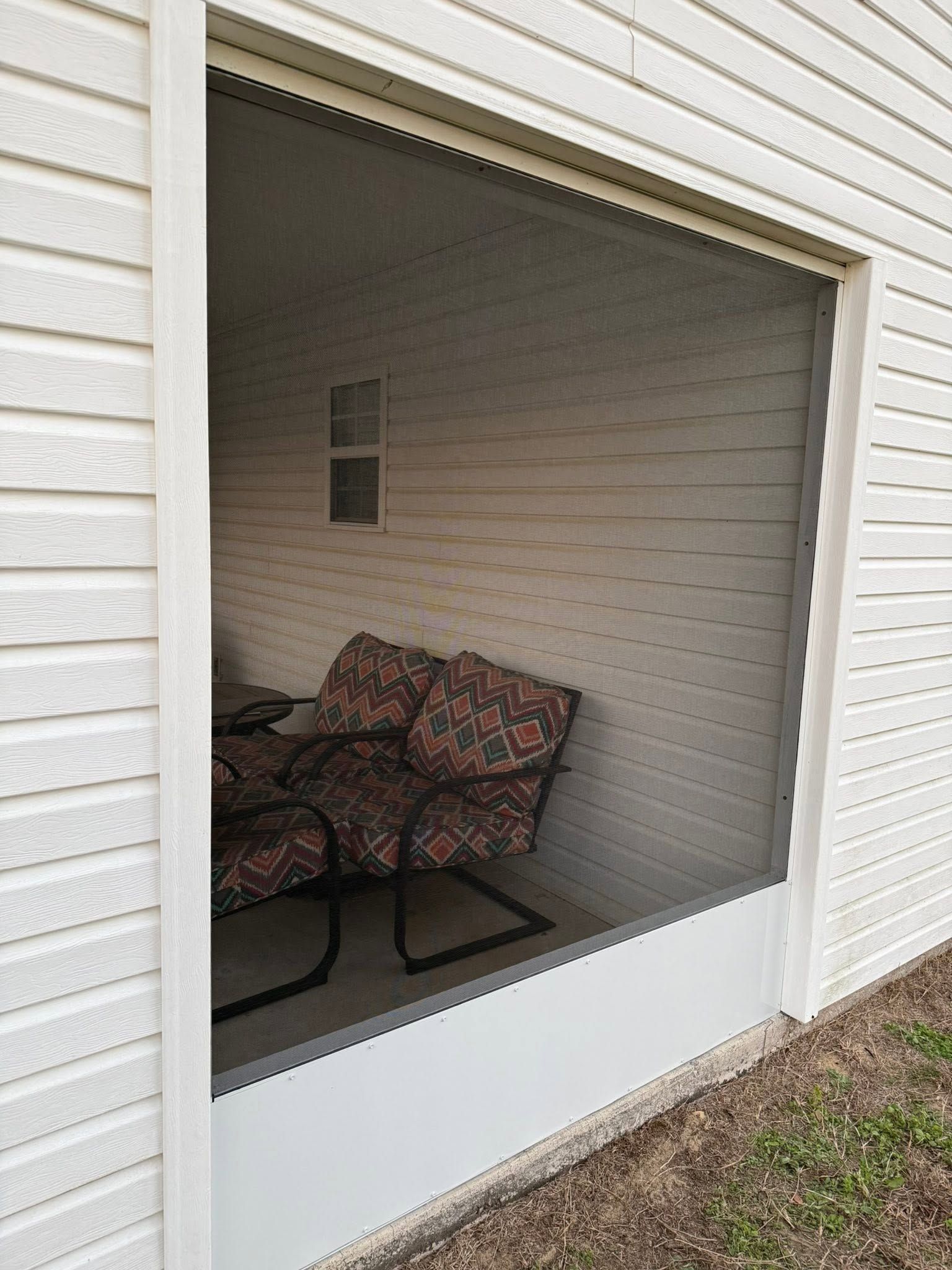 Small screened porch with white siding and patterned chairs inside.