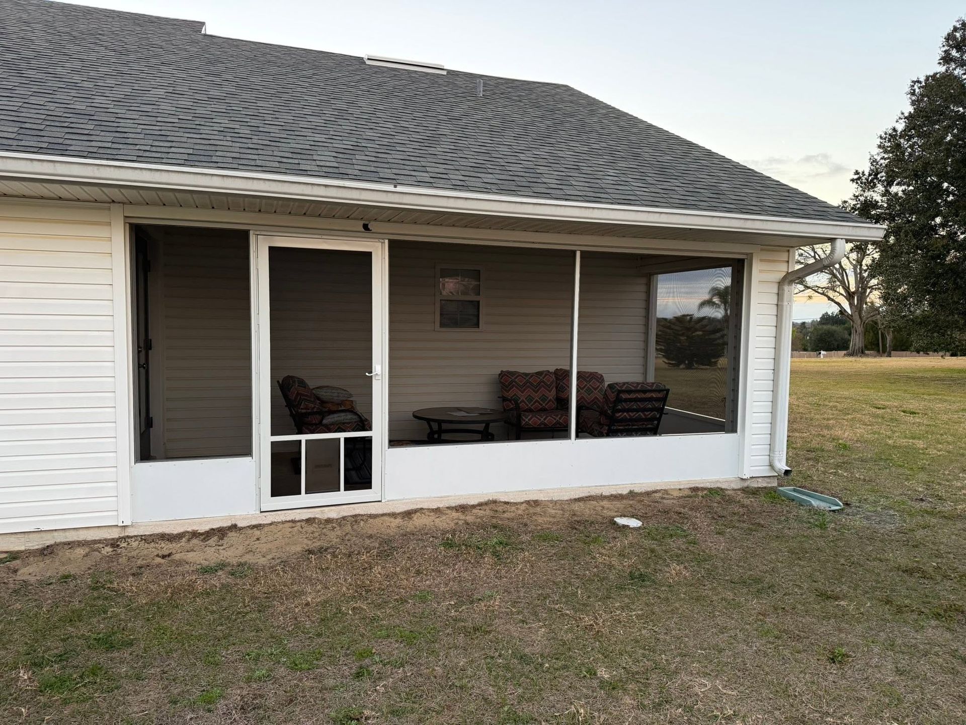 Back porch with white siding, screened windows, outdoor seating, and a grassy yard under a gray roof.