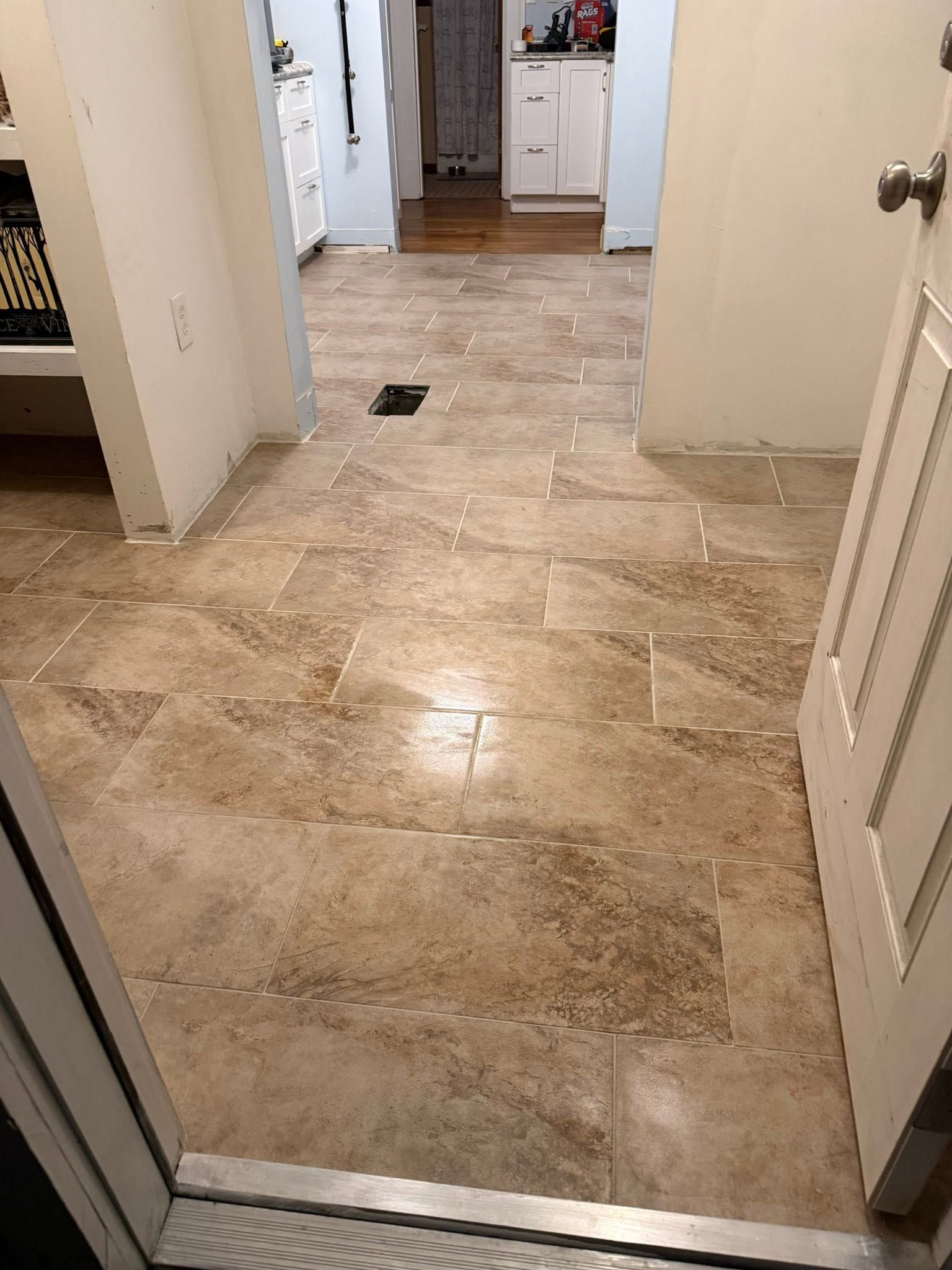 Tiled hallway leading to a kitchen, with open doors and a small dark object on the floor.