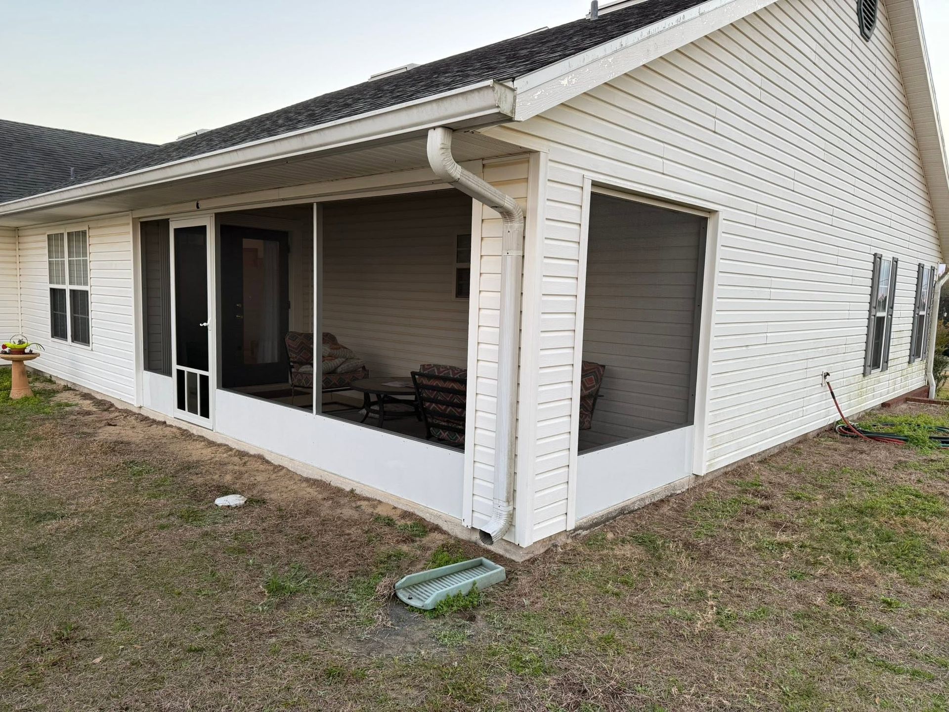 Covered porch on a white house with screened windows and a sliding glass door.