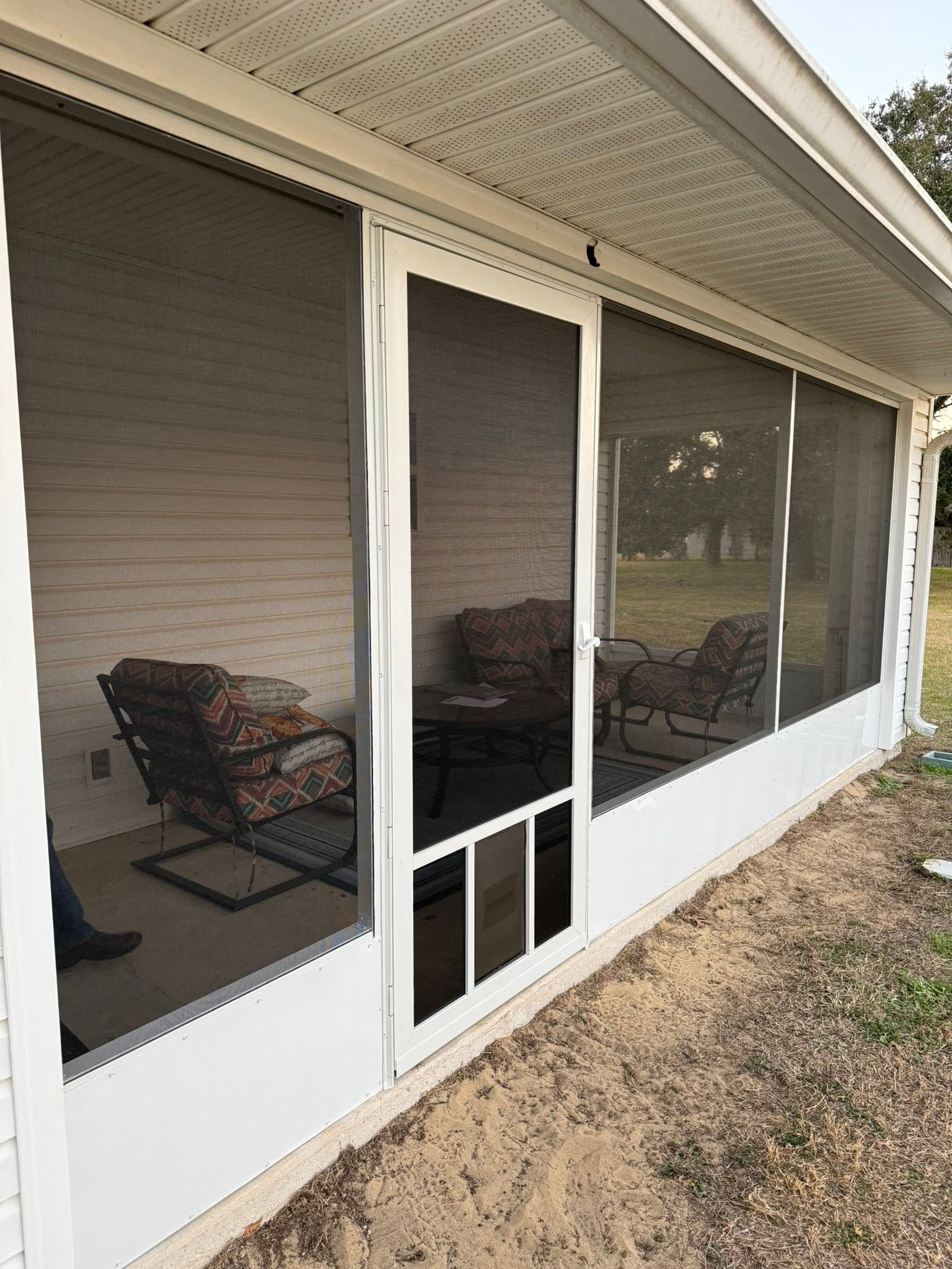 Screened porch with white frames, dark mesh panels, and outdoor chairs visible inside.