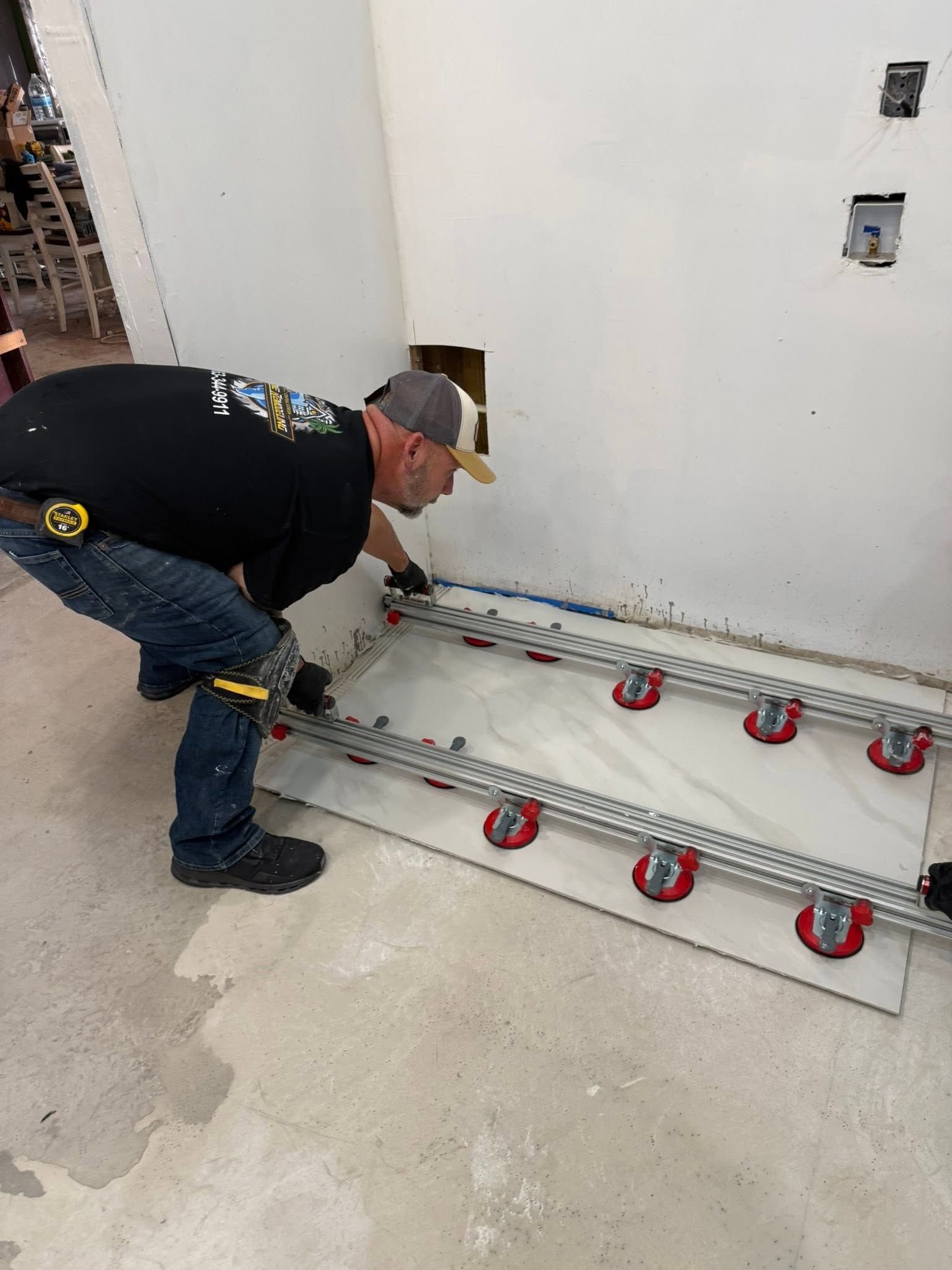 Worker installing flooring adhesive over red leveling clips in a room under construction