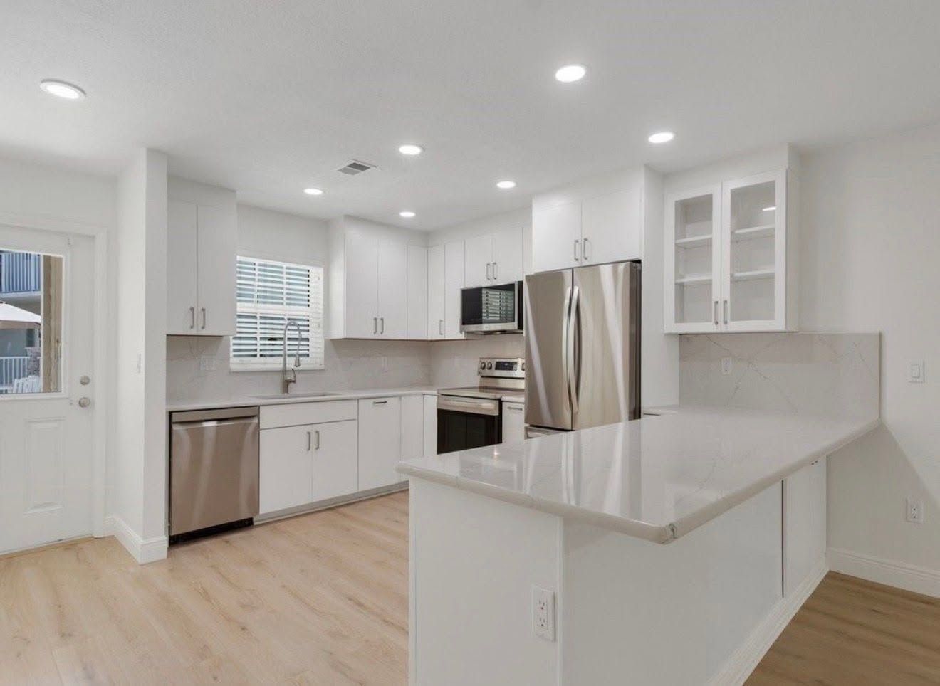Bright white modern kitchen with island, stainless appliances, and light wood floors