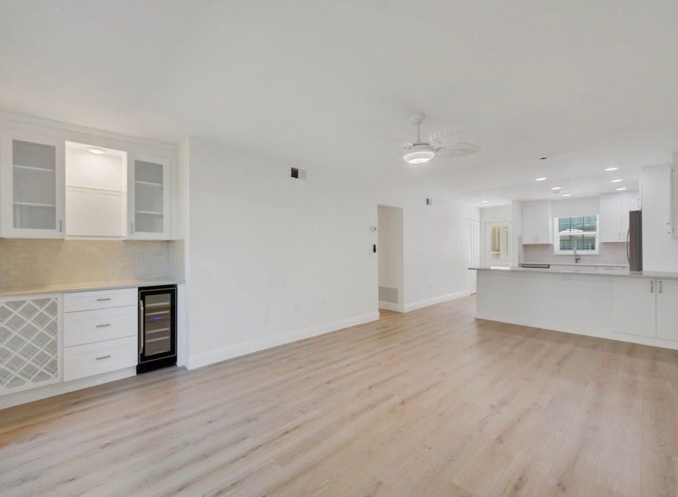 Bright empty open-plan room with light wood floors, white walls, and a kitchen bar area