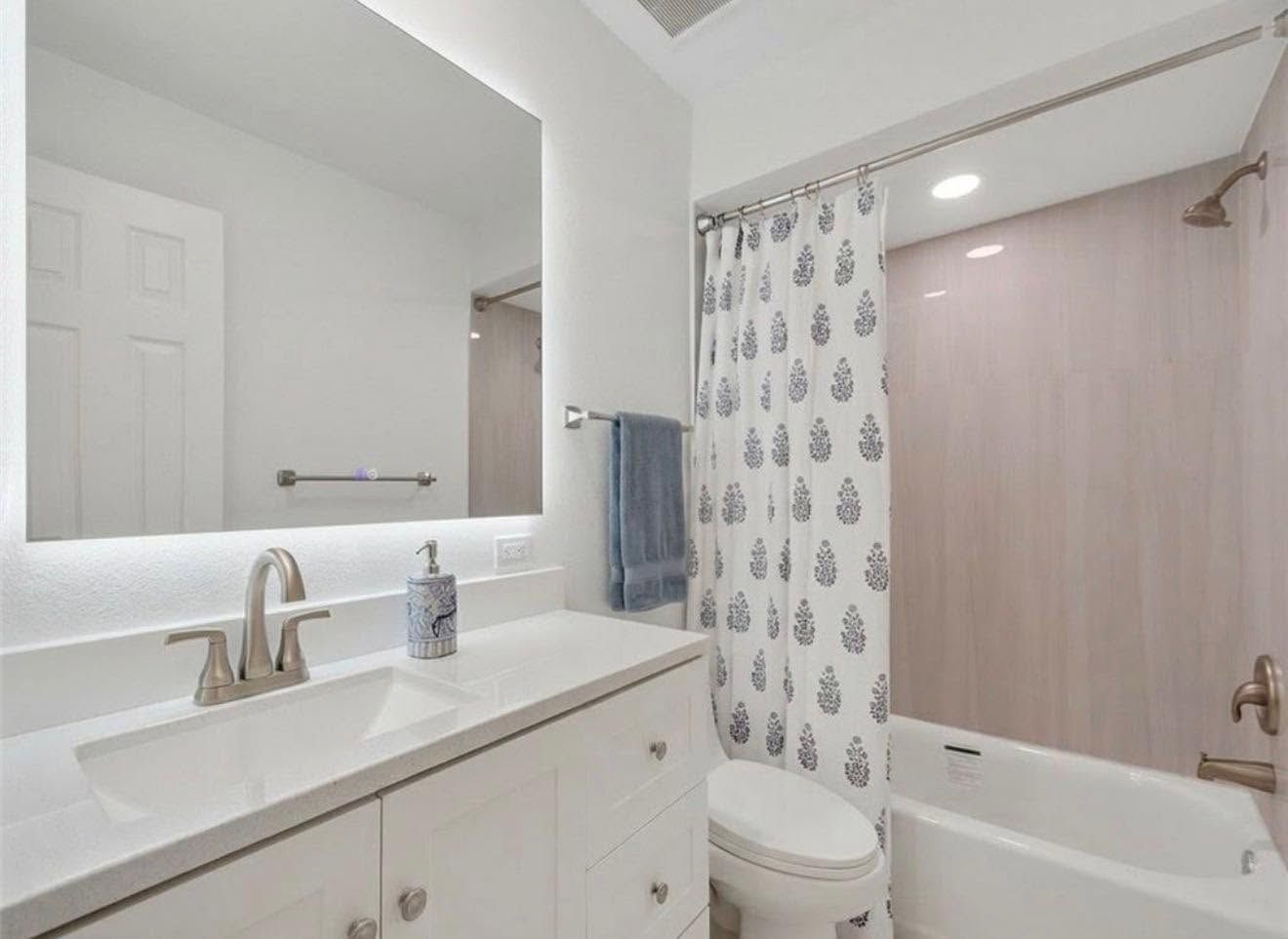 Bright bathroom with vanity mirror, white sink, toilet, bathtub, and patterned shower curtain.