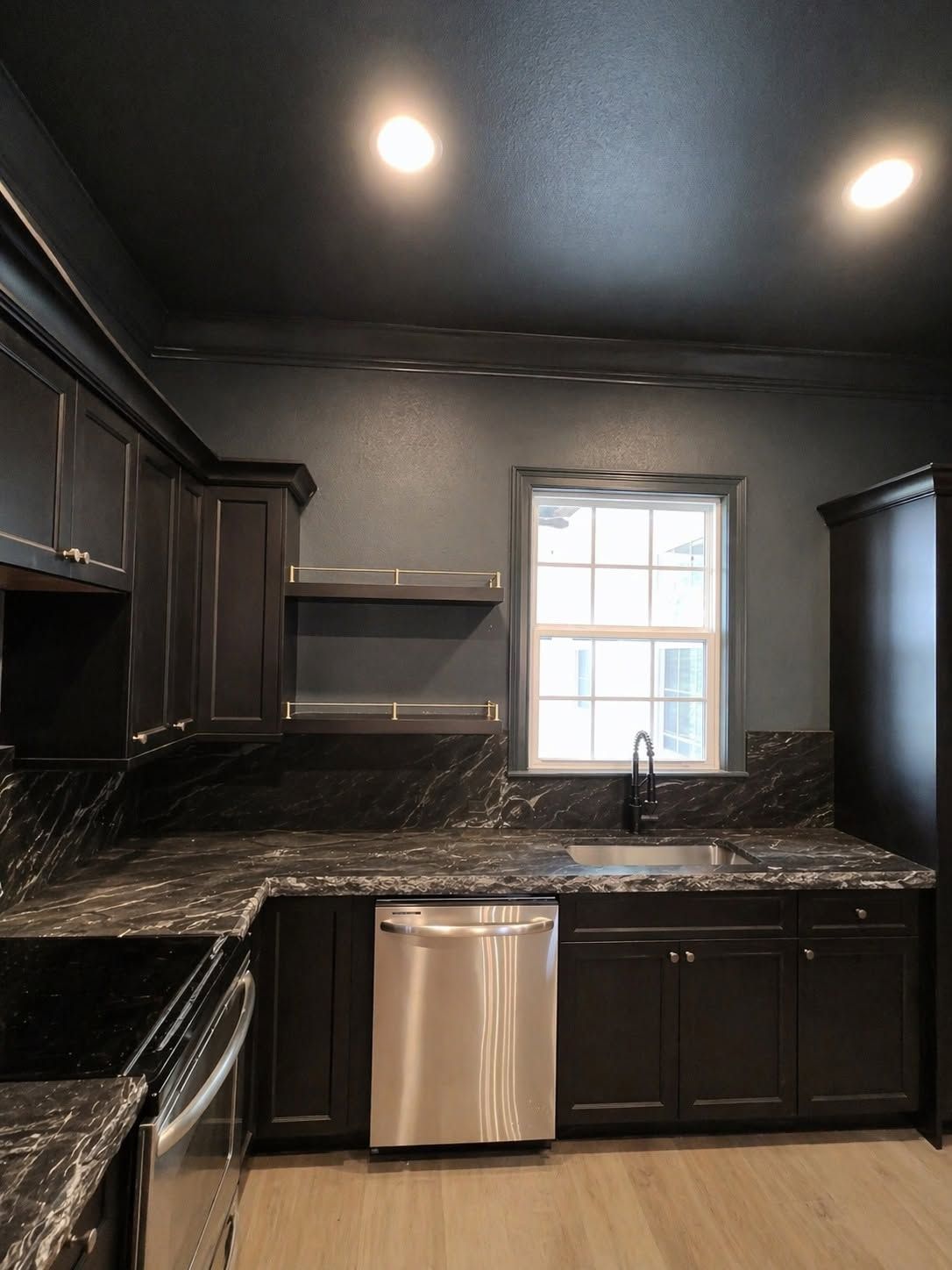 Dark modern kitchen with black cabinets, granite countertops, stainless dishwasher, and a small window.