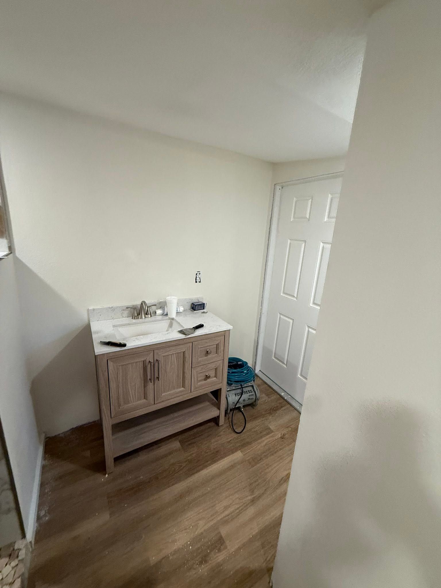 Small bathroom with a white vanity, wood cabinet, and light wood floor near a door.