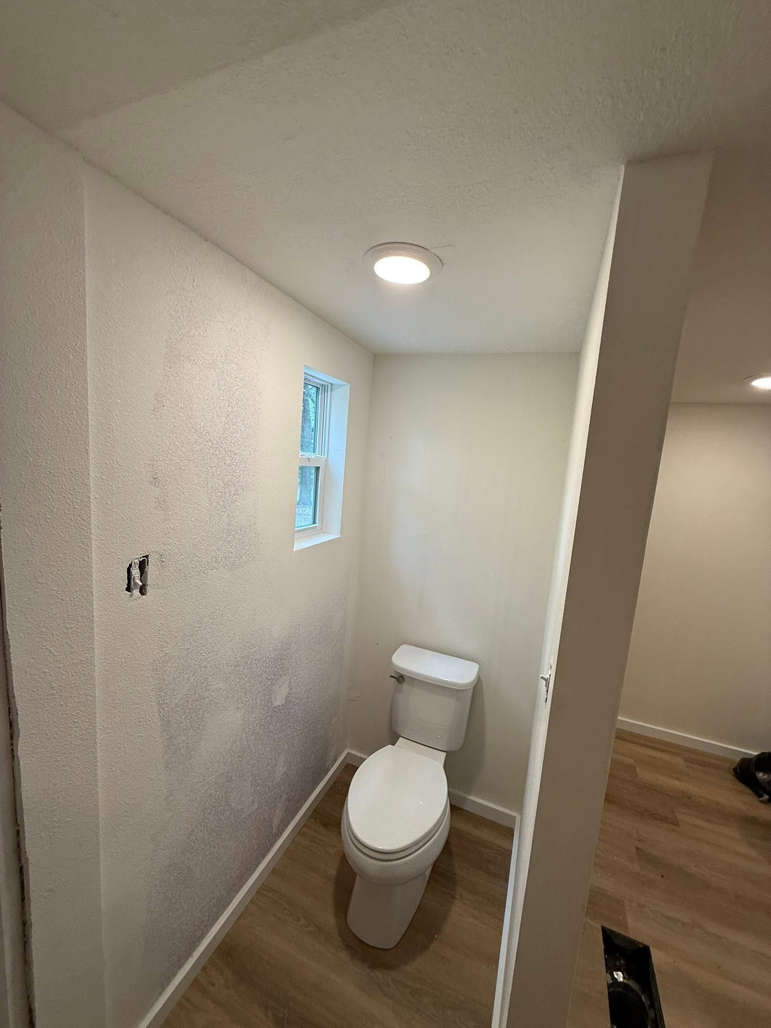 Small bathroom with a toilet, white walls, a window, and a ceiling light.