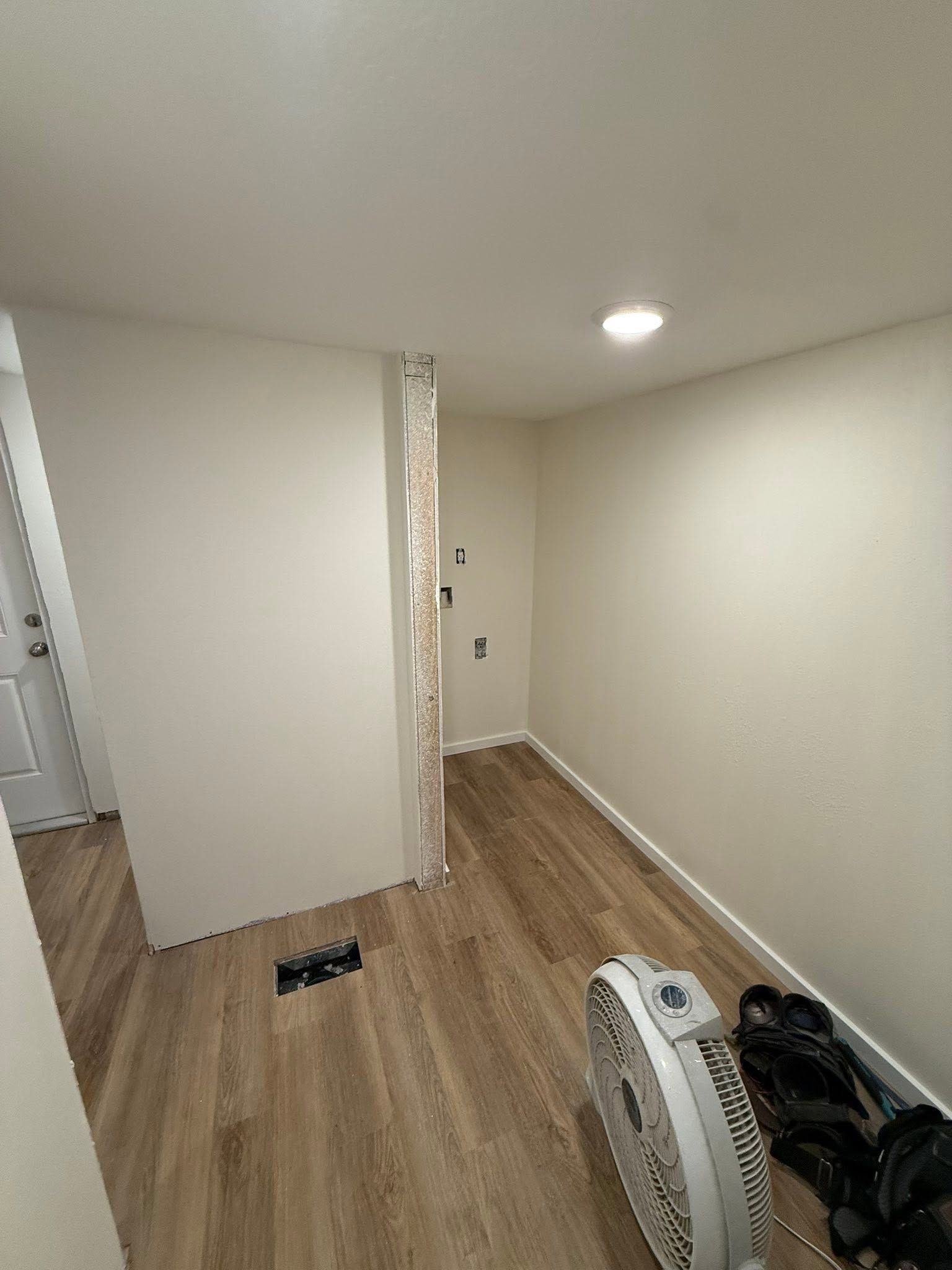 Empty hallway with wood floors, white walls, and a fan on the floor near a doorway.