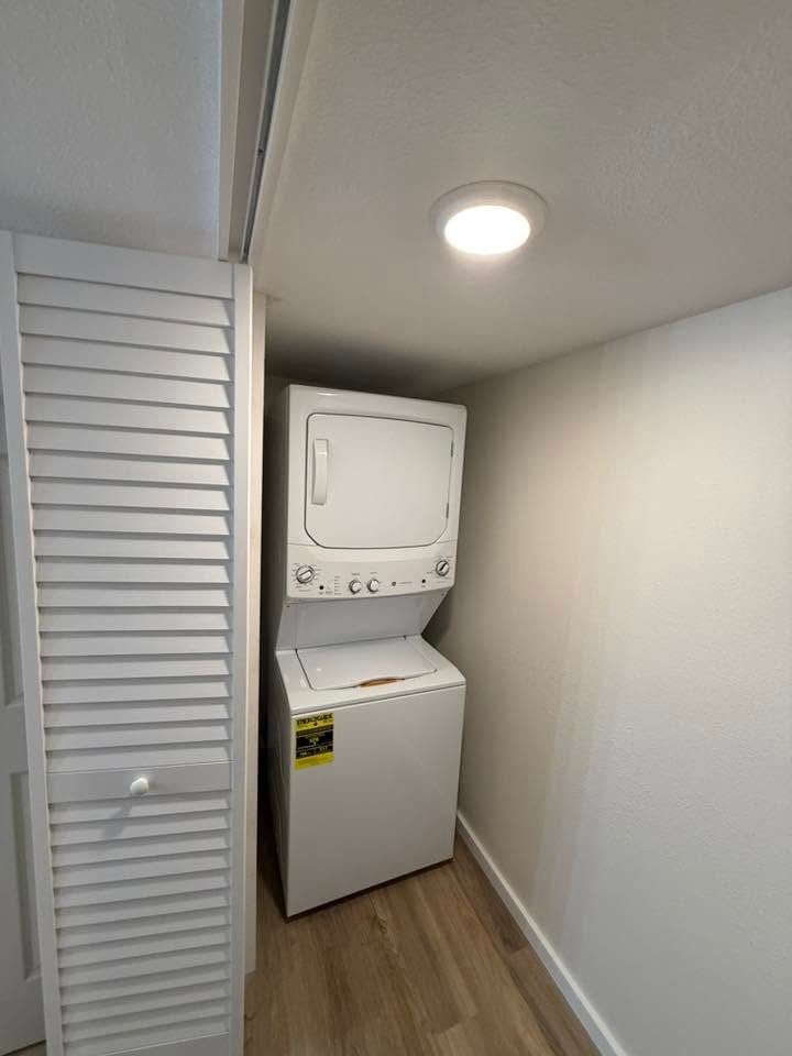 Laundry closet with a stacked washer and dryer in a narrow white hallway.