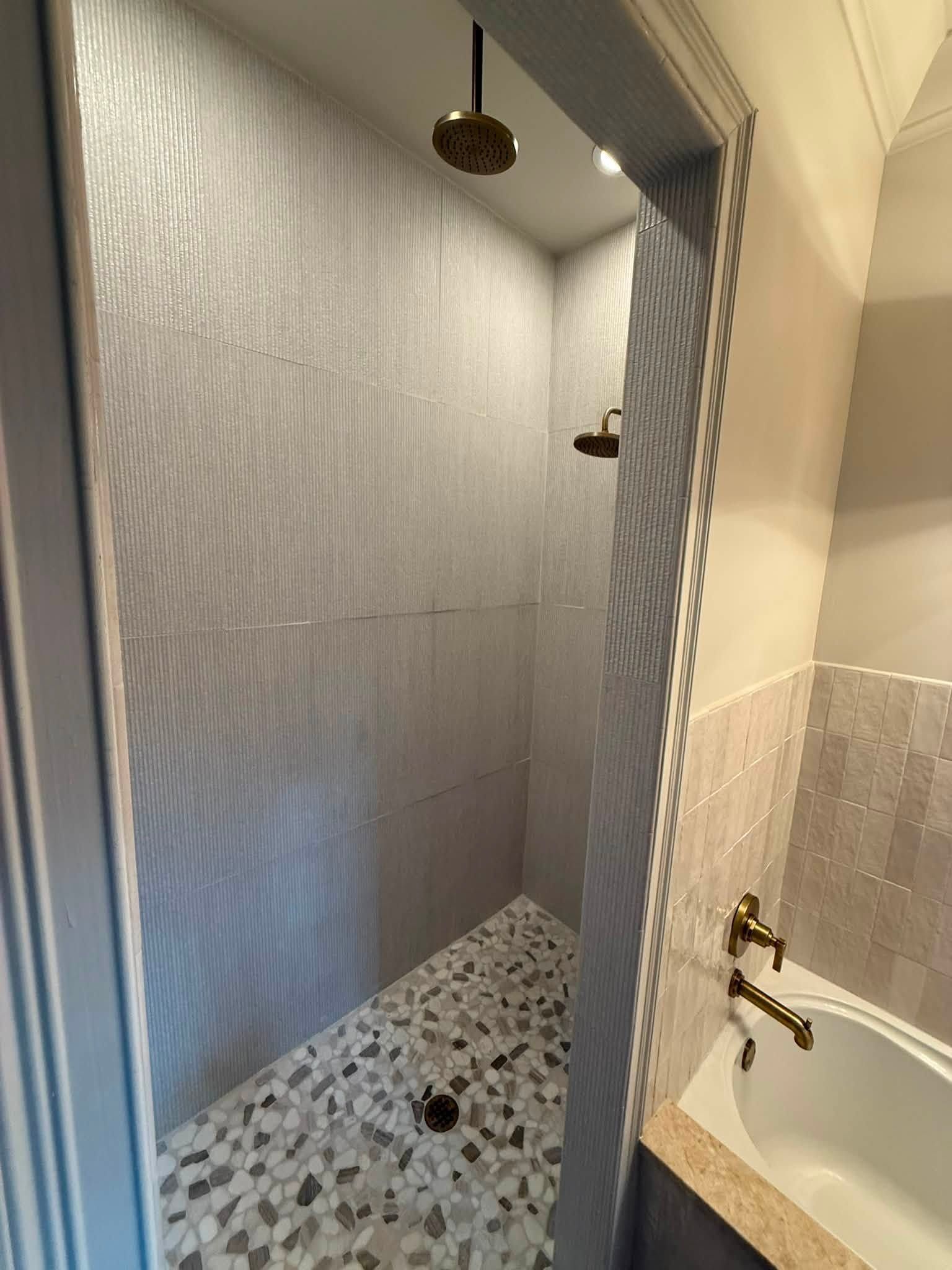 Small bathroom with a shower stall, patterned floor, and bathtub with brass fixtures