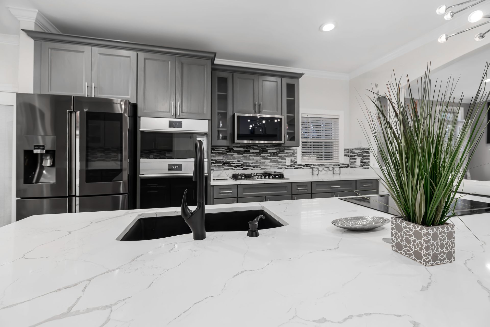 Modern kitchen with gray cabinets, stainless appliances, marble island, and a tall potted plant on the counter