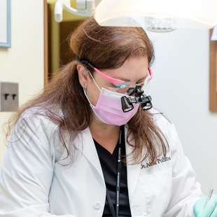 Dentist wearing pink mask and glasses, working in an office with bright lighting.