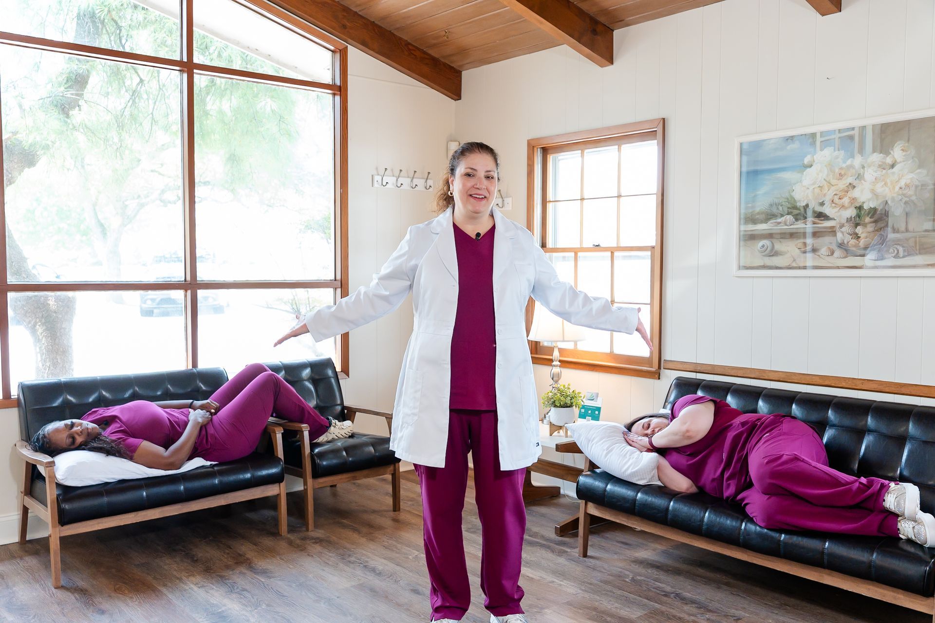 Medical professional standing with arms outstretched; two people rest on couches, indoors.