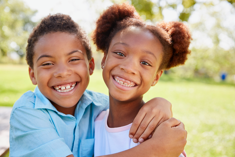 A boy and a girl are hugging each other in a park.