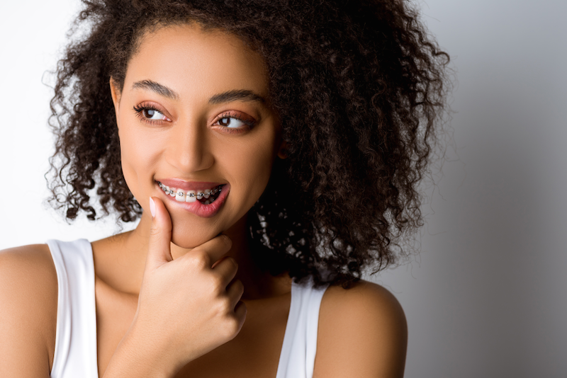 A woman with braces on her teeth is smiling and touching her chin.