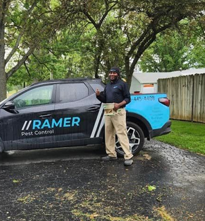Pest control worker standing beside a Ramer Pest Control truck in a wooded driveway