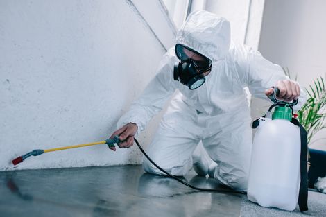 Worker in white protective suit spraying a floor with a hose and chemical sprayer.