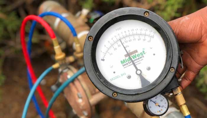 Close-up of a gauge connected to pipes, displaying a pressure reading. Red and blue hoses attached.