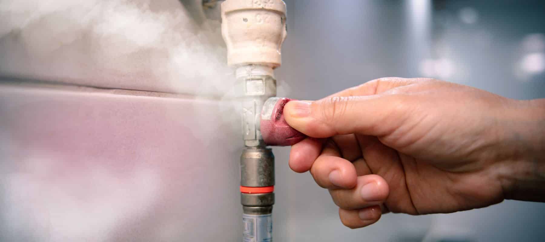 A hand turning a red valve on a metal pipe, steam billowing out.