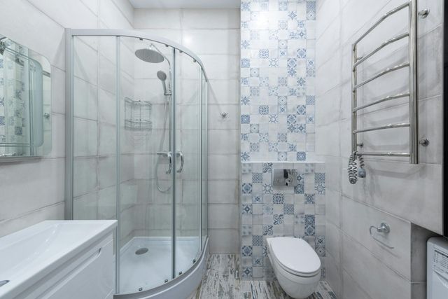 Small, modern bathroom with a glass shower, toilet, and towel rack; blue and white tile accents.