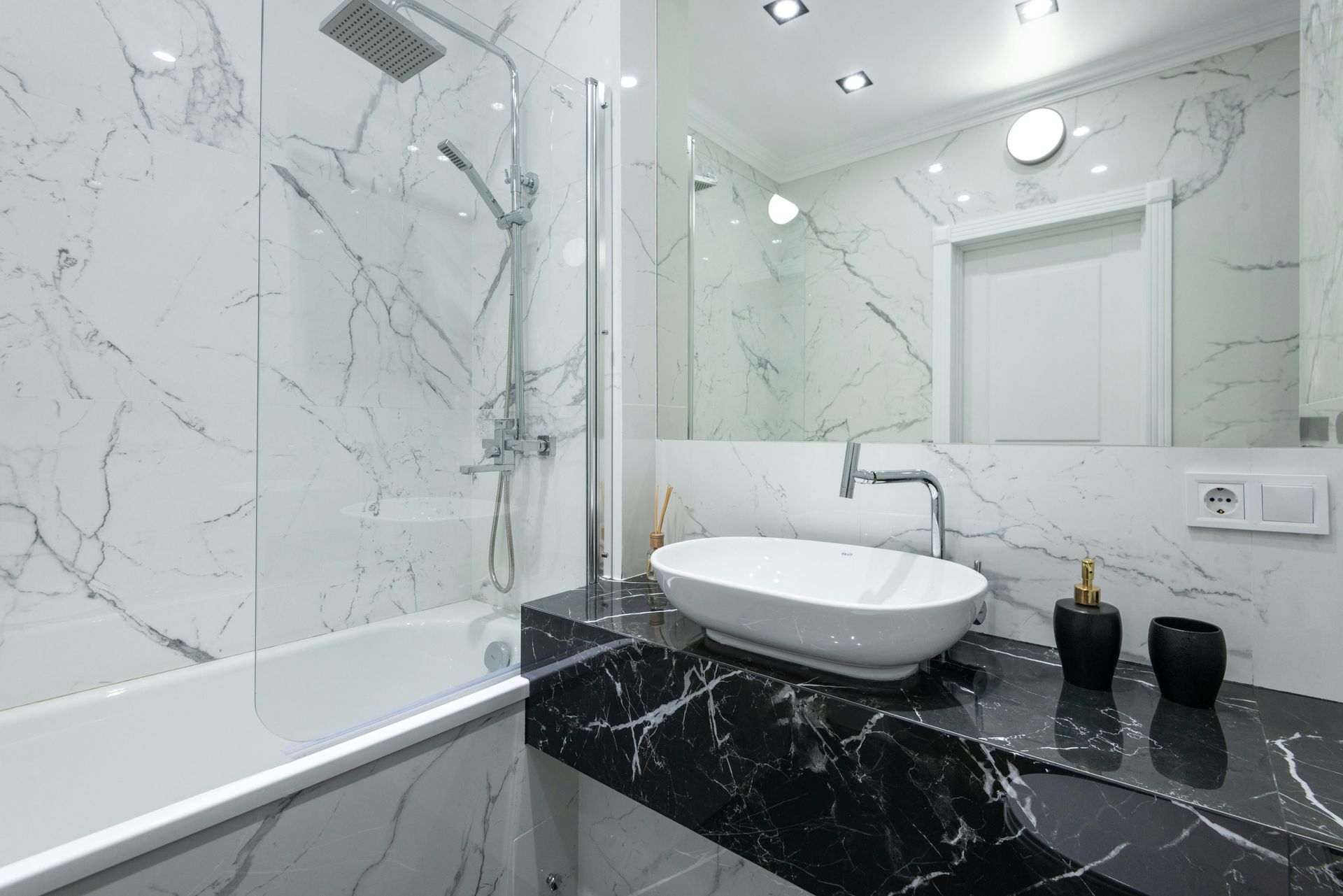 Modern bathroom with white marble walls, black marble countertop, and a white sink.