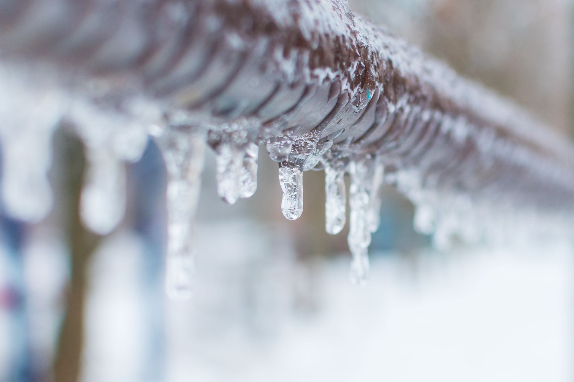 Close-up of a brown pipe with small, clear icicles hanging from it. Winter setting.