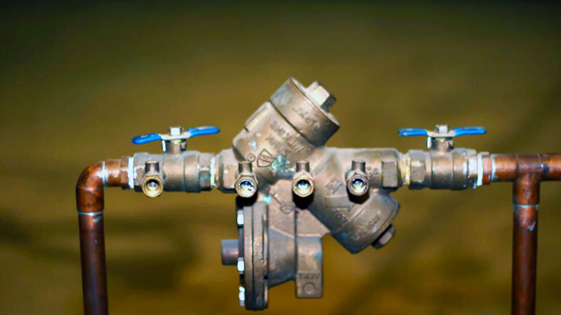 Backflow preventer valve with copper pipes and blue-handled shutoff valves.