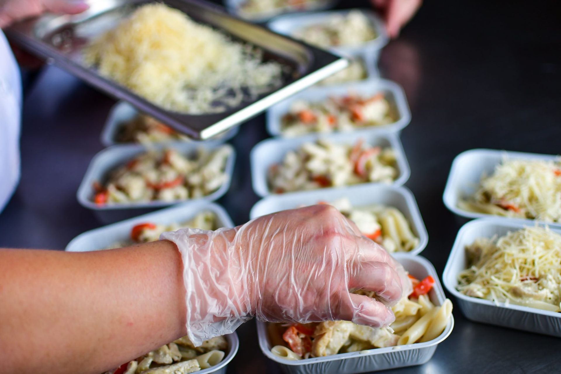 Gloved hand placing food into takeout containers at a catering buffet