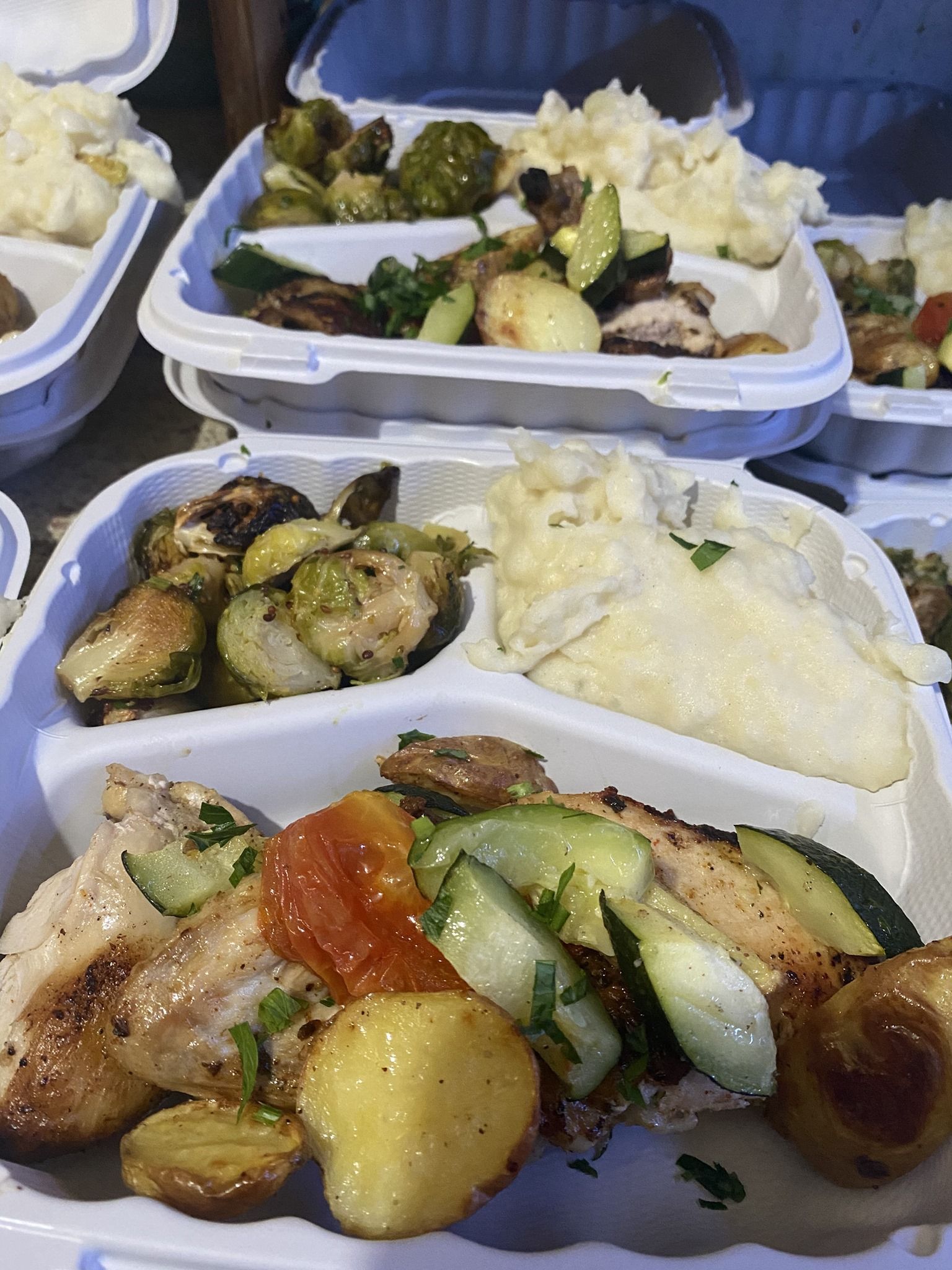 Takeout containers of food with grilled vegetables, potatoes, and rice on a table