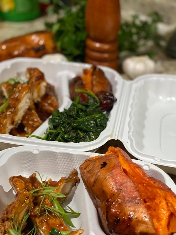 Takeout containers with glazed roasted chicken and sautéed greens on a table