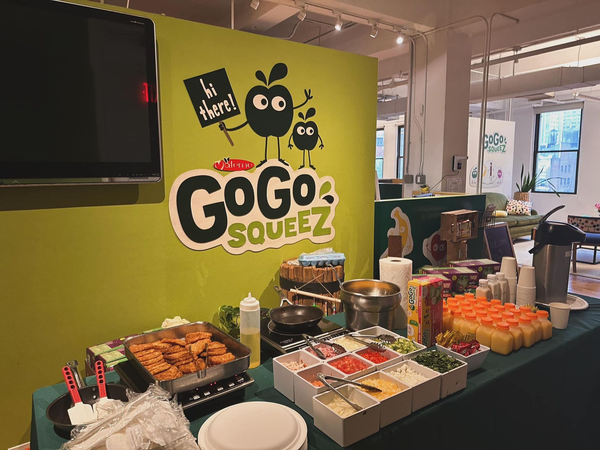 GoGo squeeZ snack display with fruit cups, apples, and branded green backdrop in a store.