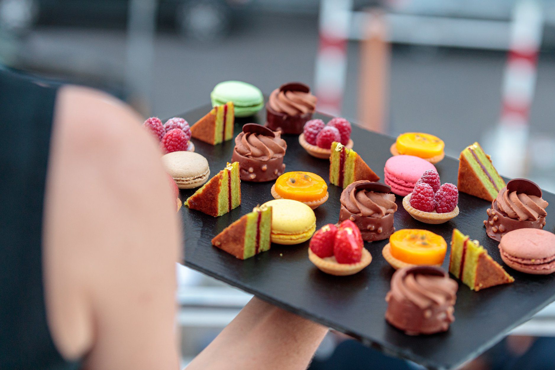 Tray of colorful assorted pastries and macarons being held outdoors