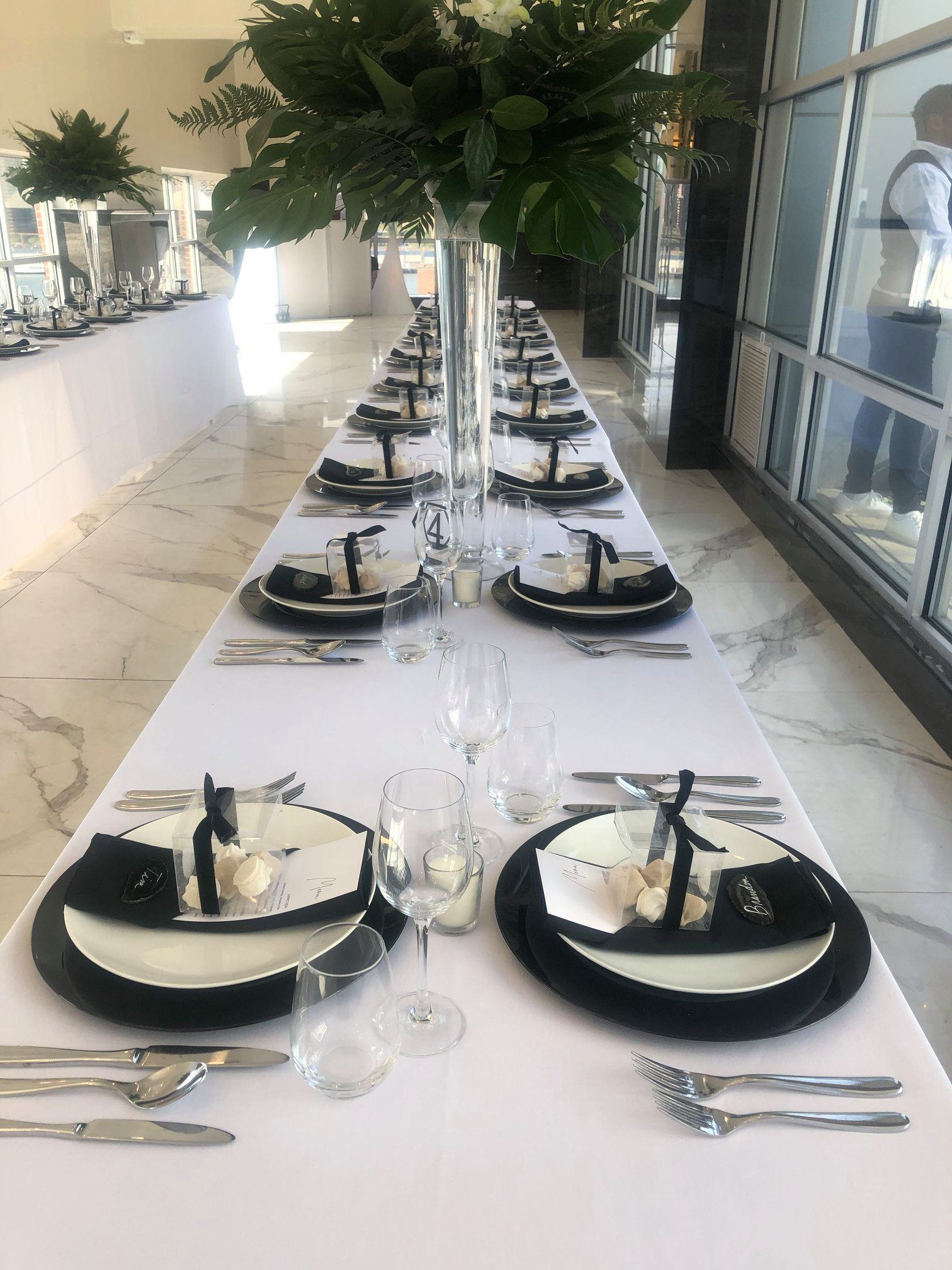 Long banquet table set with black-and-white place settings and lush floral centerpieces in a bright room