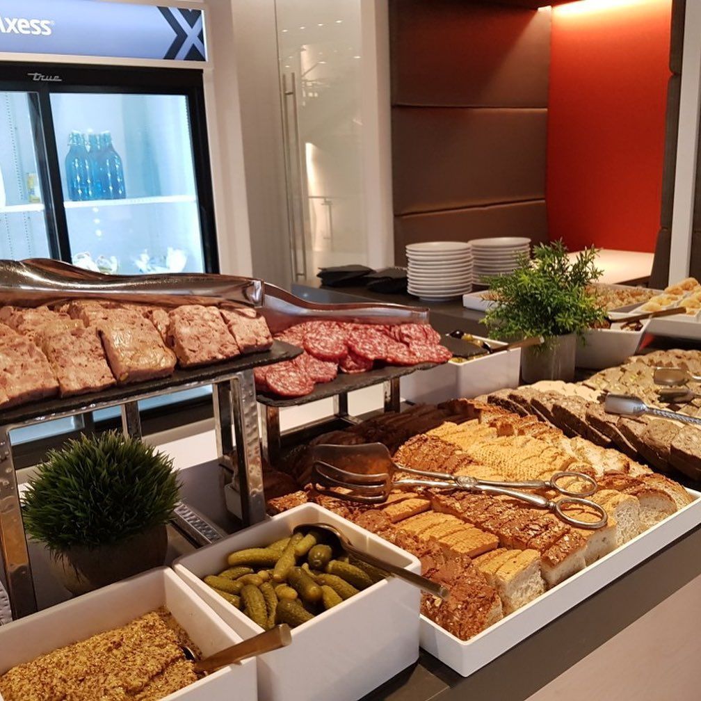 Buffet counter with assorted breads, meats, pickles, and cheeses in a bright dining area