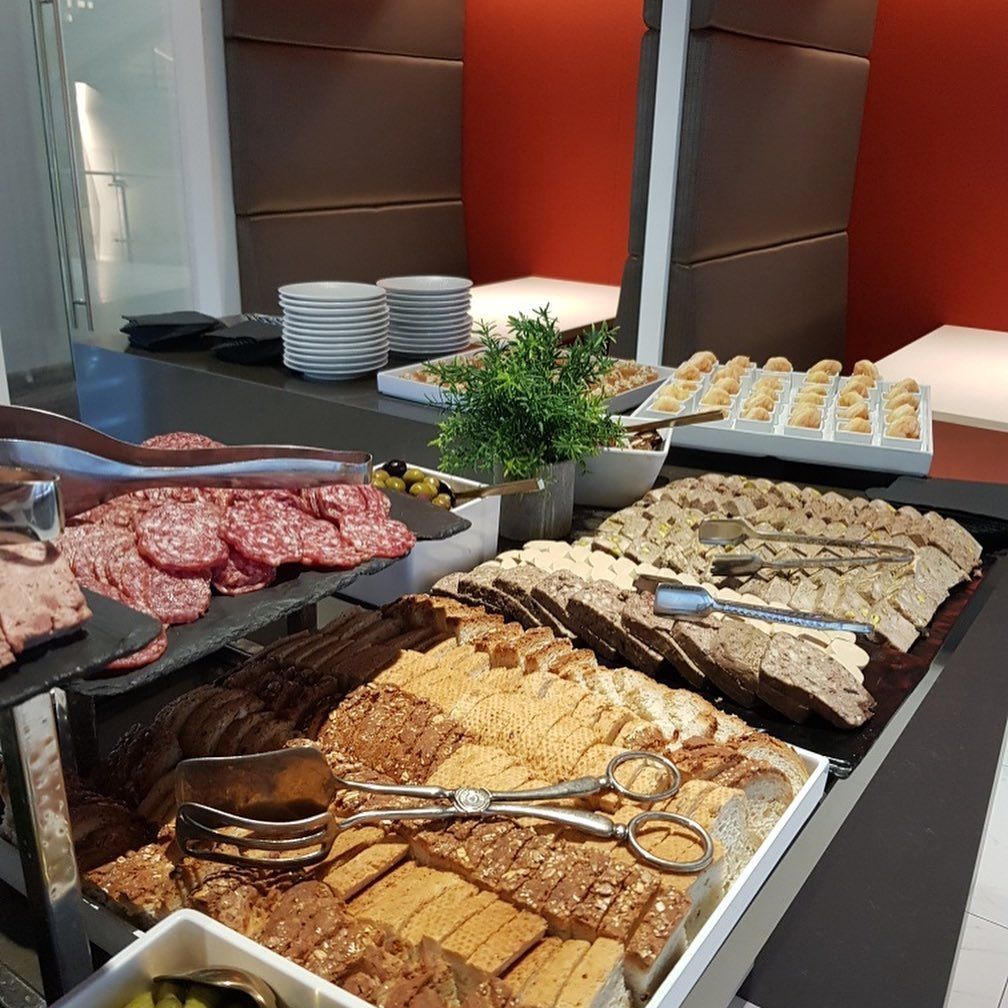 Buffet table with sliced meats, bread, crackers, and pastries arranged in trays at a restaurant