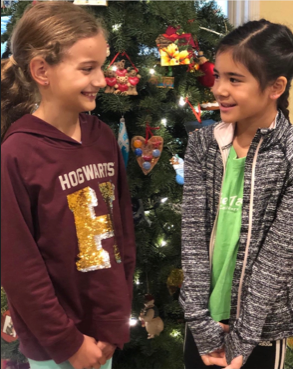 Two children smiling beside a decorated Christmas tree.