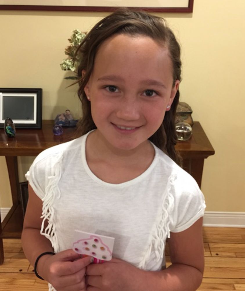 Smiling child in a white shirt holding a small card indoors in front of a table