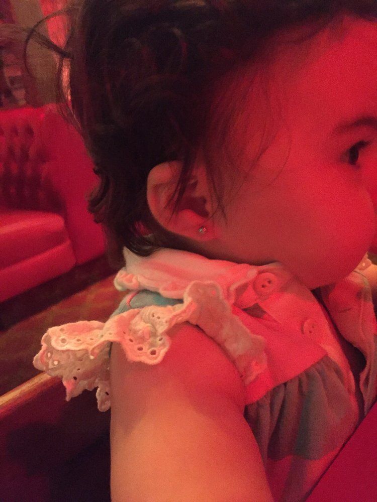 Young child in a ruffled dress, shown in side profile under warm red lighting.