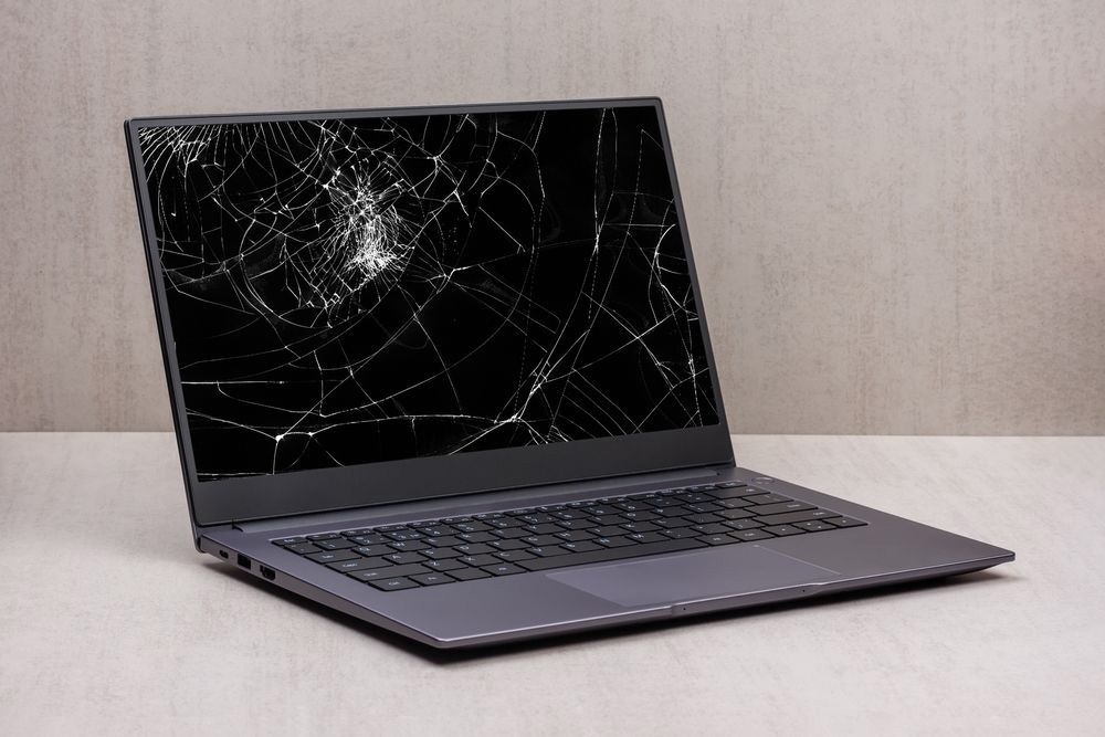 Laptop With A Broken Screen In Cracks On A Gray Background — Essential Computer Repairs In Sunshine Coast QLD