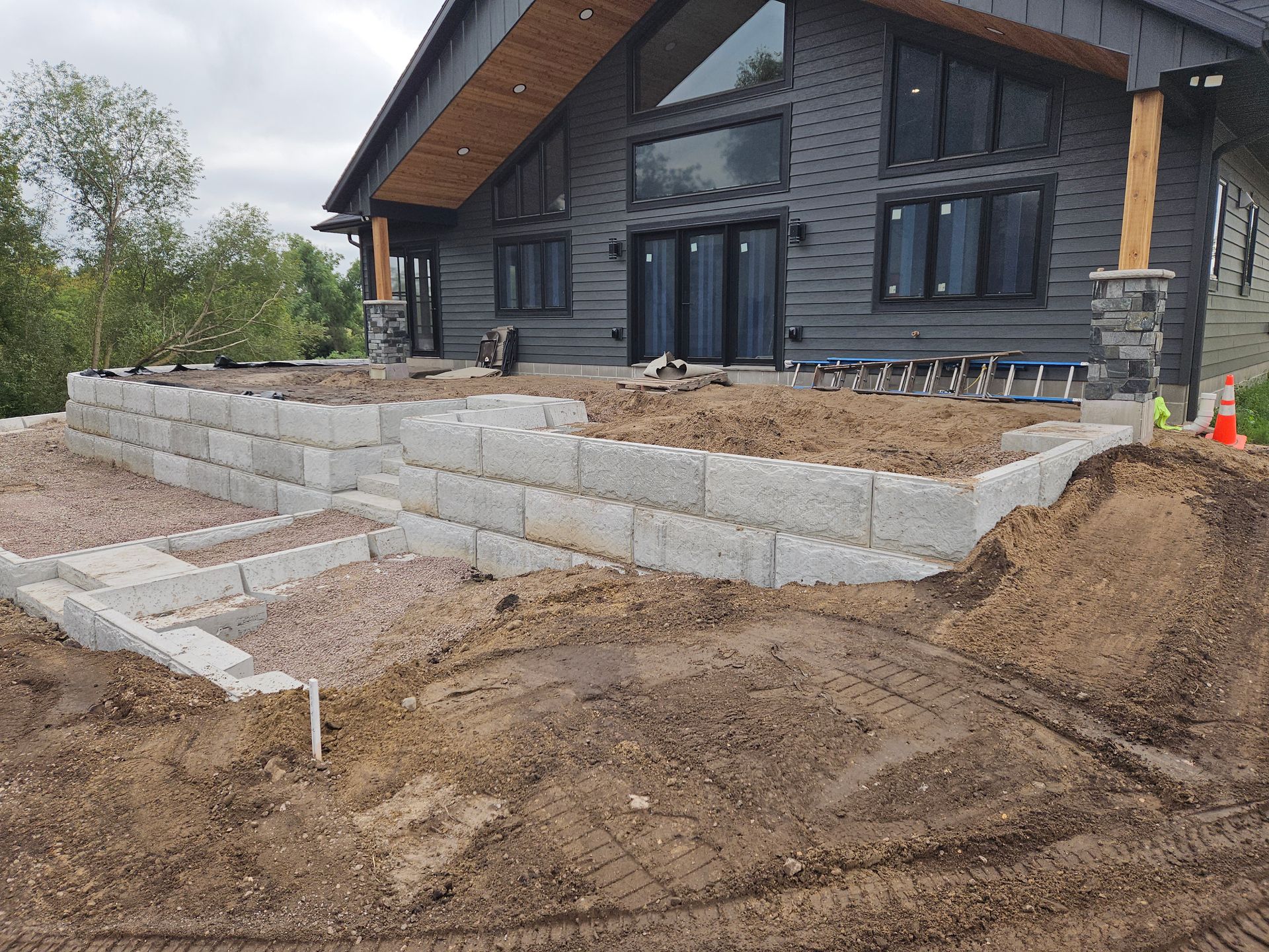 New stone retaining walls and steps under construction beside a dark gray house