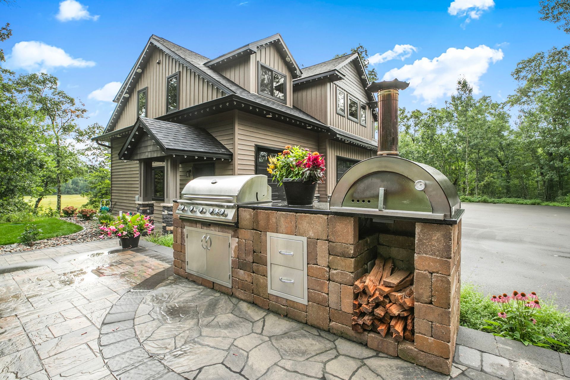 Brick outdoor pizza oven with arched wood storage in front of a large suburban house